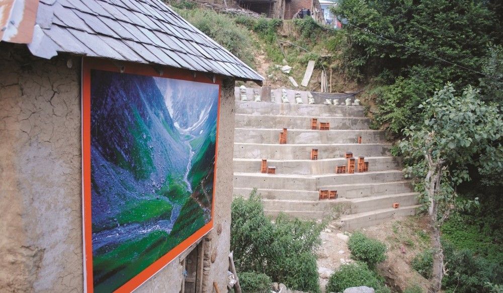 Colorful painting displayed on a rustic wall at Gunehar Village Art Gallery in Bir Billing, surrounded by greenery and hillside steps.