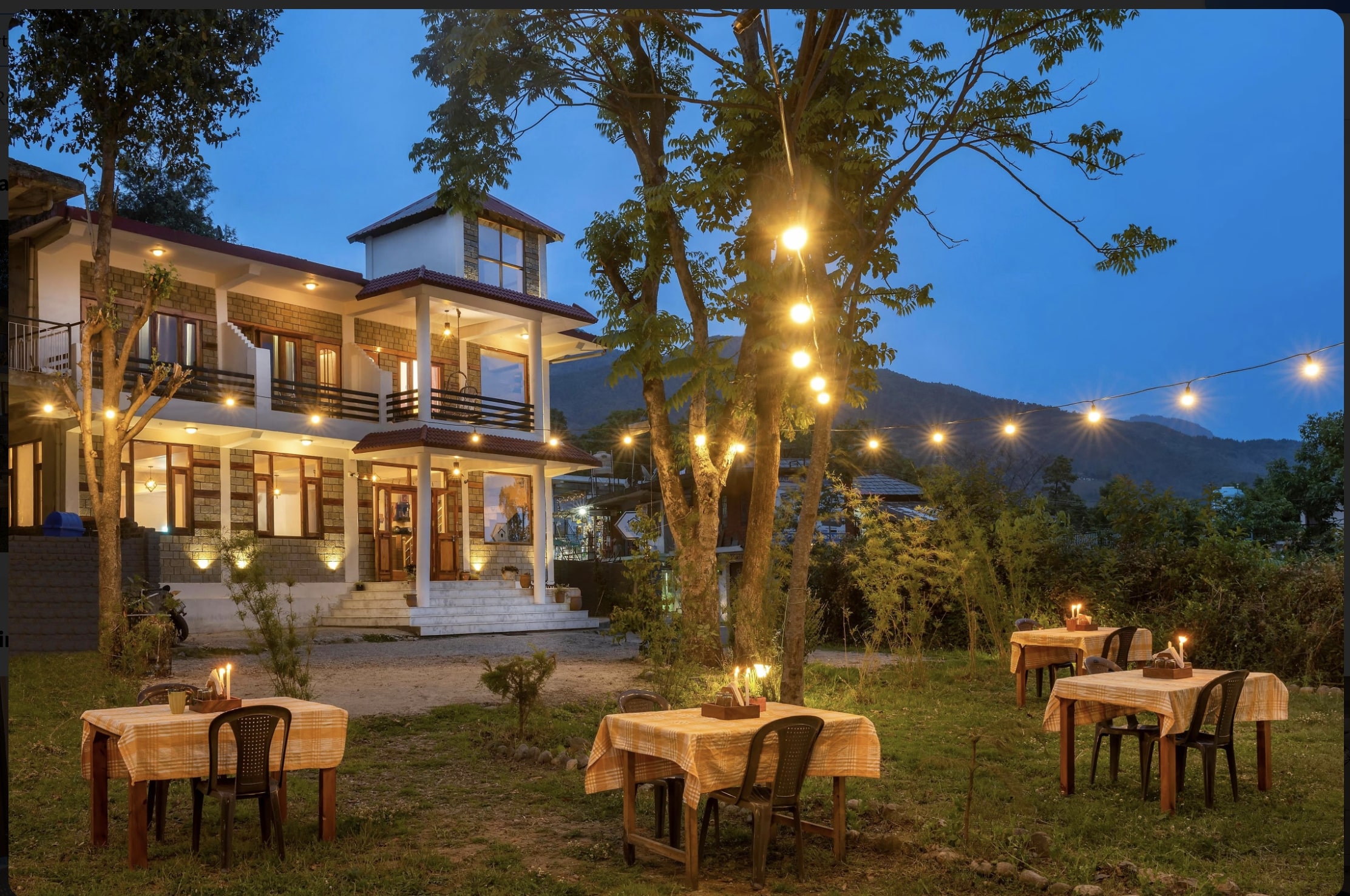 Evening view of The Birdhouse Villa in Bir Billing with outdoor dining setup, warm lights, and mountain backdrop.